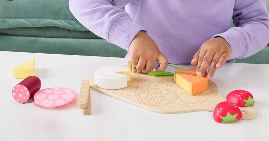 girl playing with a wooden charcuterie board set on a table