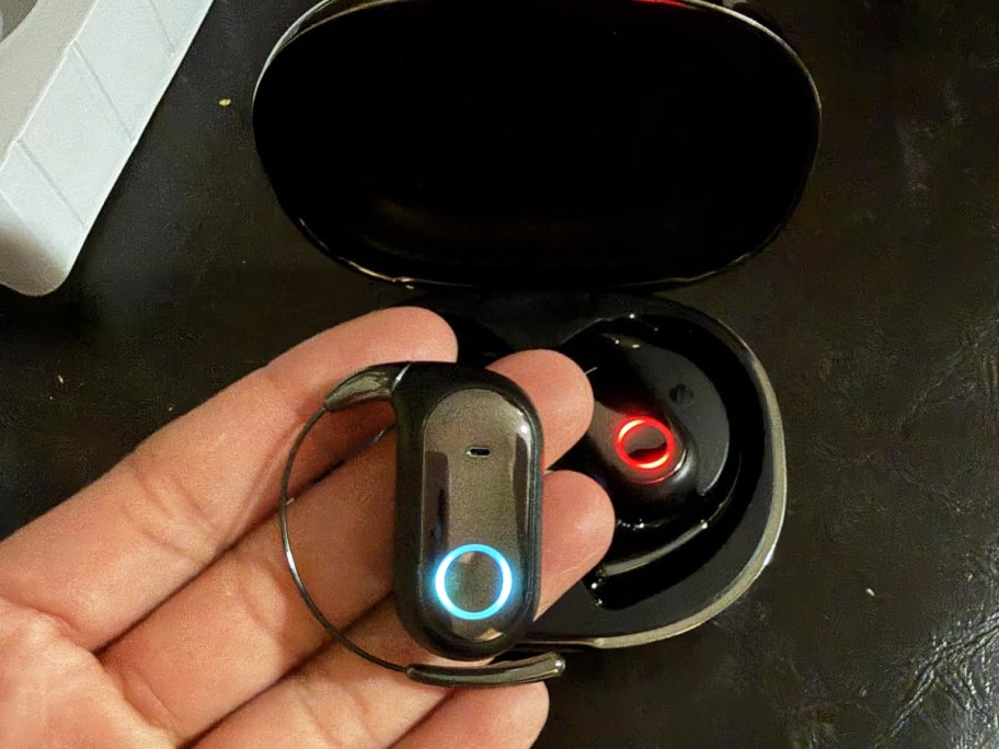 hand holding a black earbud with charging case in background