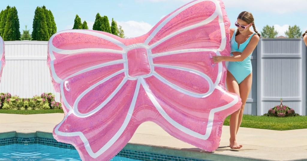 Woman holding giant pink bow shaped pool, float, and standing next to pool