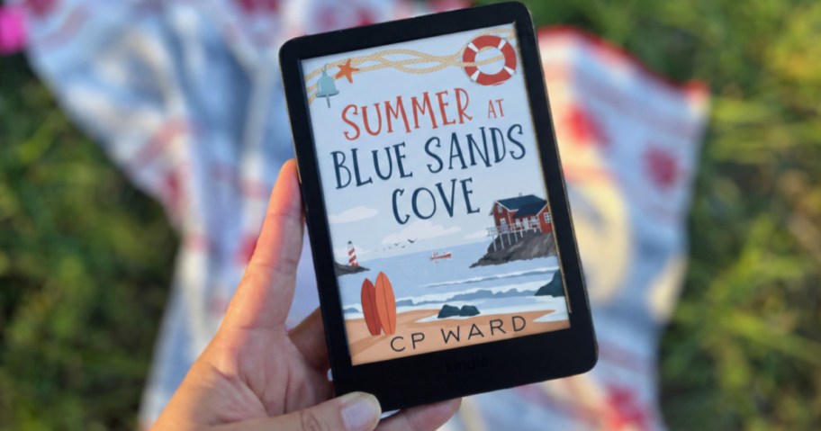 Hand holding Kendall with summer blue Sands Cove on the cover
