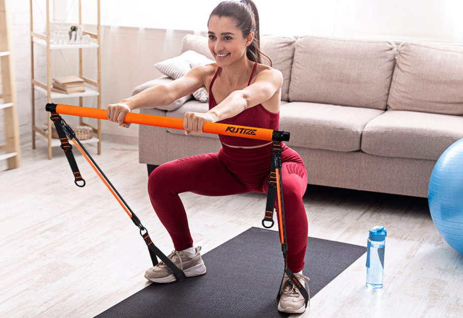 woman squatting using an orange and black pilates bar