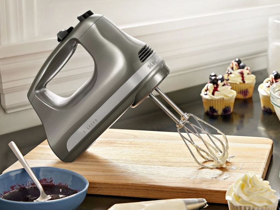 A silver KitchenAid Hand Mixer on a cutting board