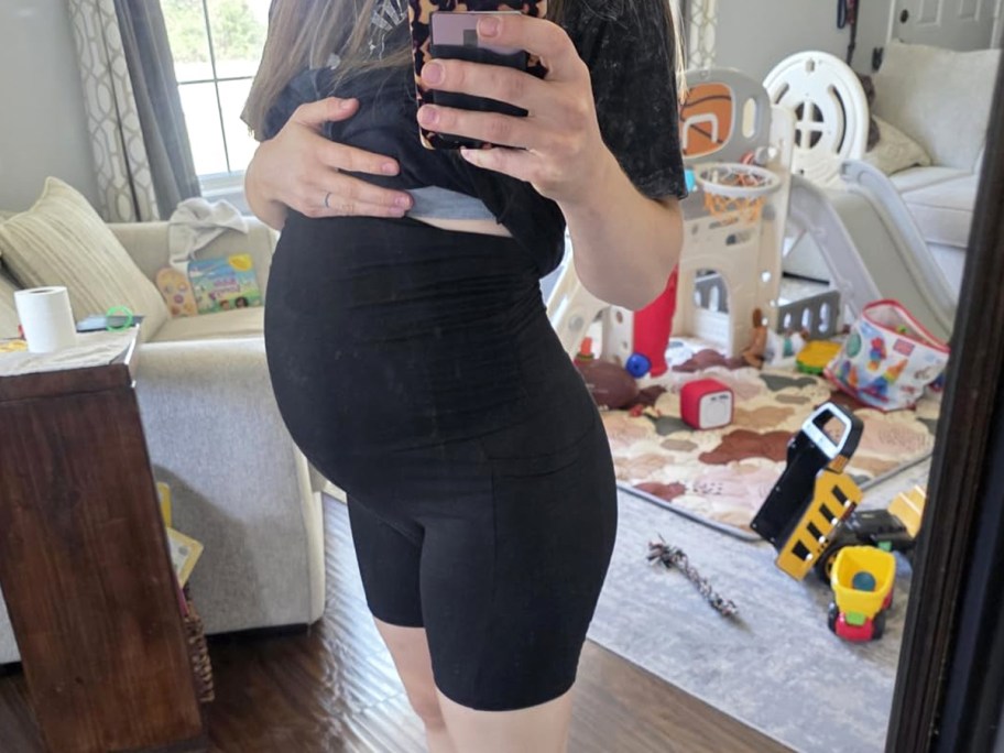 woman taking photo in mirror wearing black top and black maternity shorts