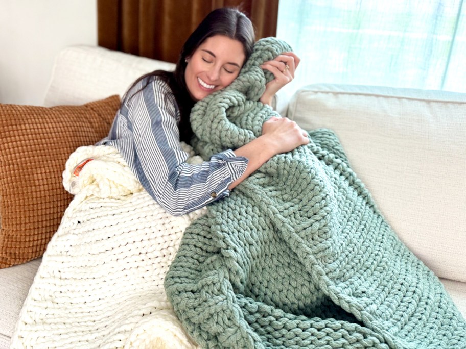 woman on couch hugging a green chunky knit throw blanket