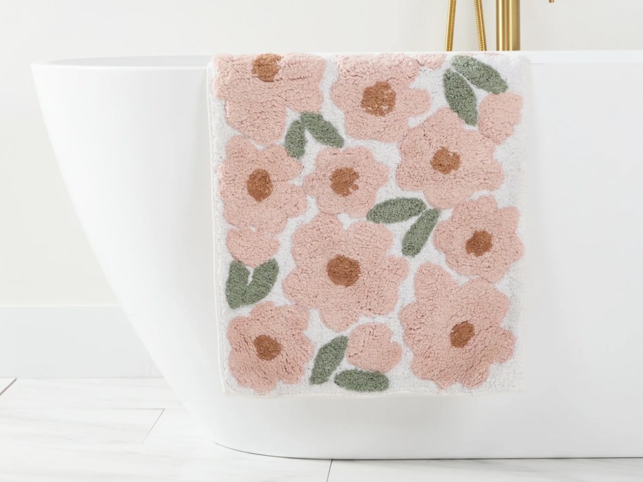 pink floral print bath mat hanging on side of tub