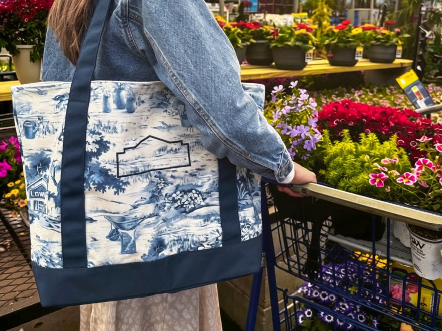 woman wearing a Lowe's tote while pushing a shopping cart in a garden center