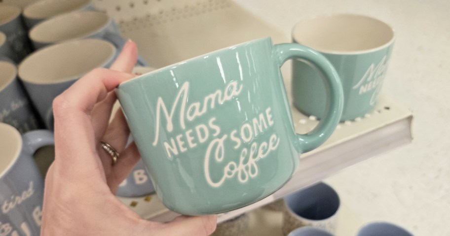 hand holding a green mug that says "Mama Needs Some Coffee"