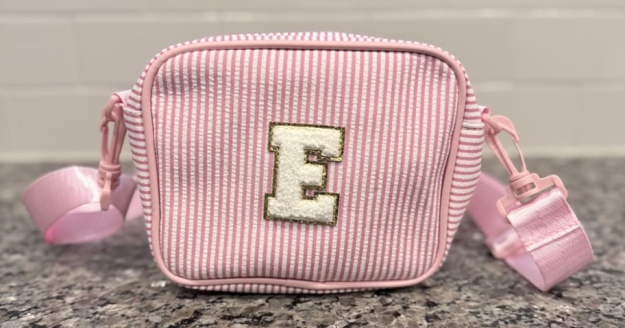 pink striped crossbody bag with letter e stitched on front sitting on the counter