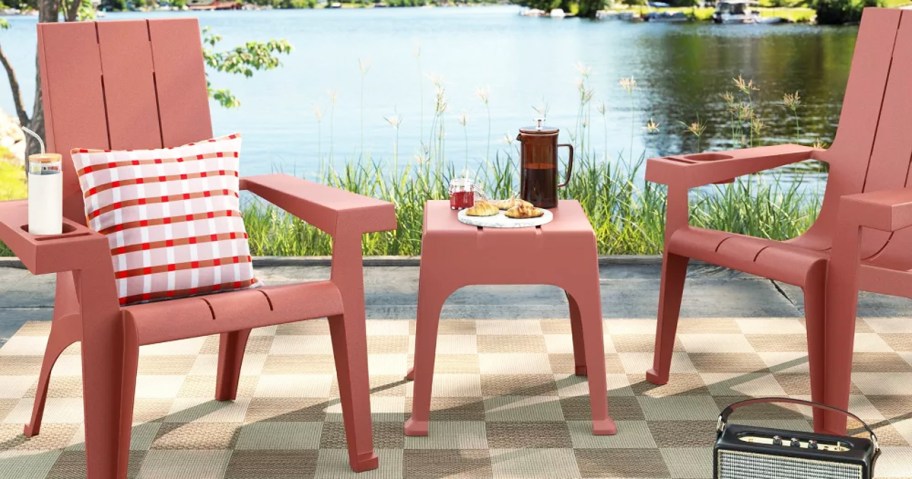 red Adirondack Chairs and matching table near lake