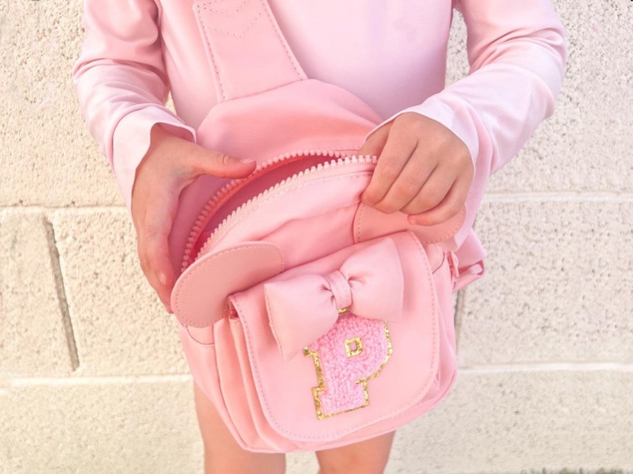 little girl wearing a pink initial sling bag with mouse ears