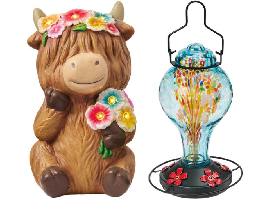 A cute, smiling cow figurine adorned with colorful flowers sits next to a vibrant, multicolored glass lantern.