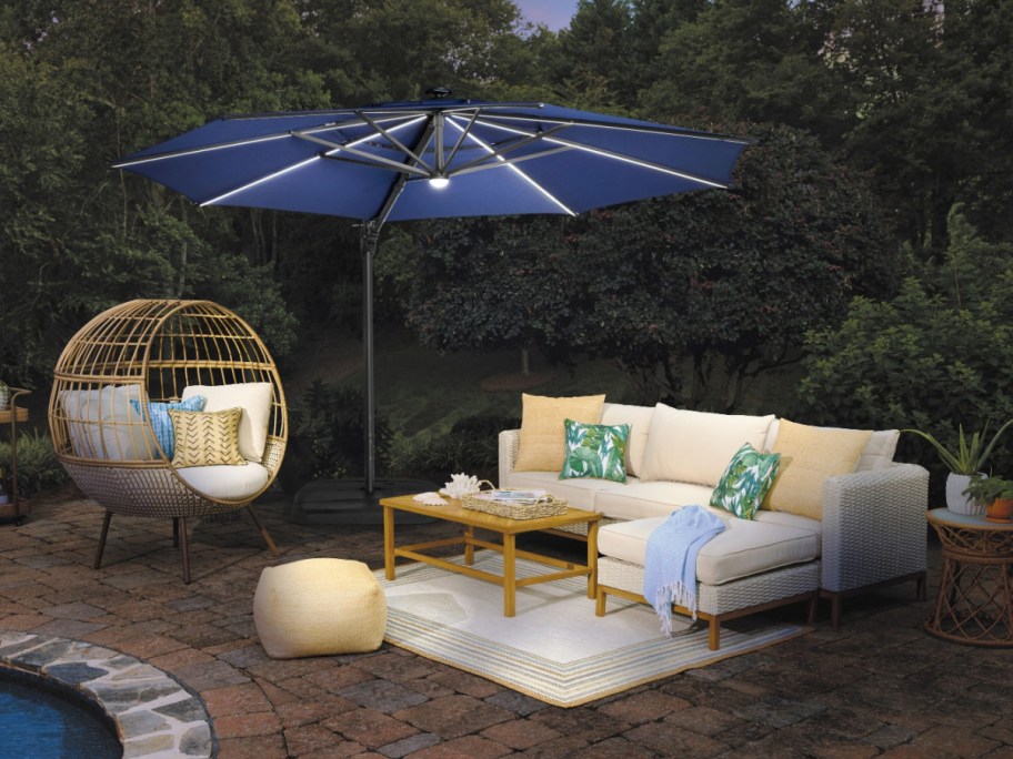 Outdoor patio with wicker furniture. Cozy cream couch with colorful pillows is under a blue umbrella.