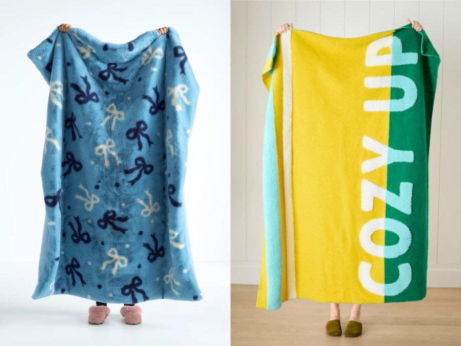 Two people holding up large blankets: one blue with a ribbon pattern and the other yellow with "COZY UP" printed on it.