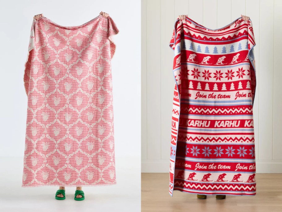 Two people holding up oversized blankets, one in a red and white checkered pattern and the other in a red and white holiday-themed design, standing side by side.
