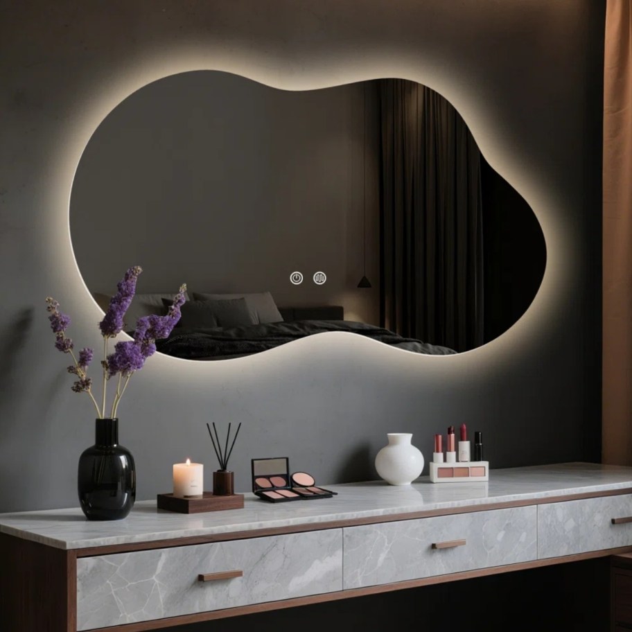 irregular shaped backlight mirror on a wall above a console table