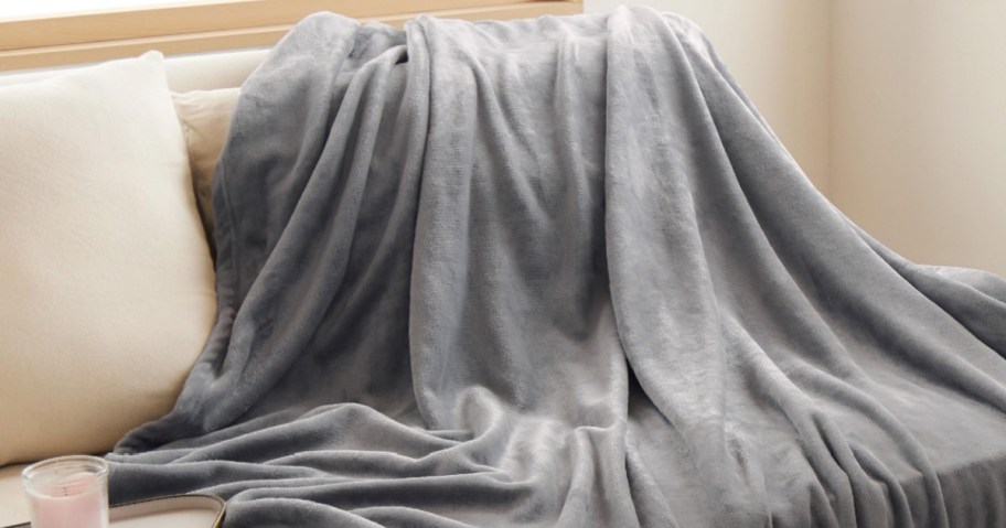 A soft gray blanket drapes over a white sofa. A small candle sits nearby.