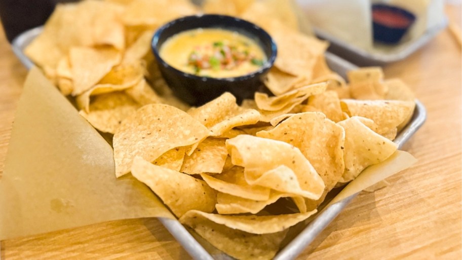 a basket of nachos with a cup of queso