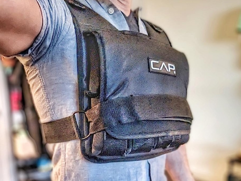 Person wearing a black weighted vest labeled "CAP" over a light blue shirt, indoors.