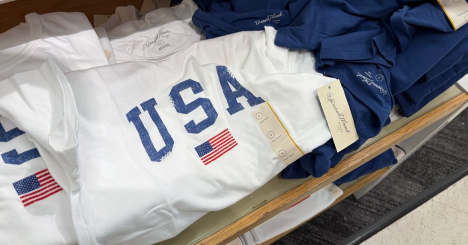 A display of T-shirts, one white with "USA" printed on it and an American flag, alongside other blue shirts.