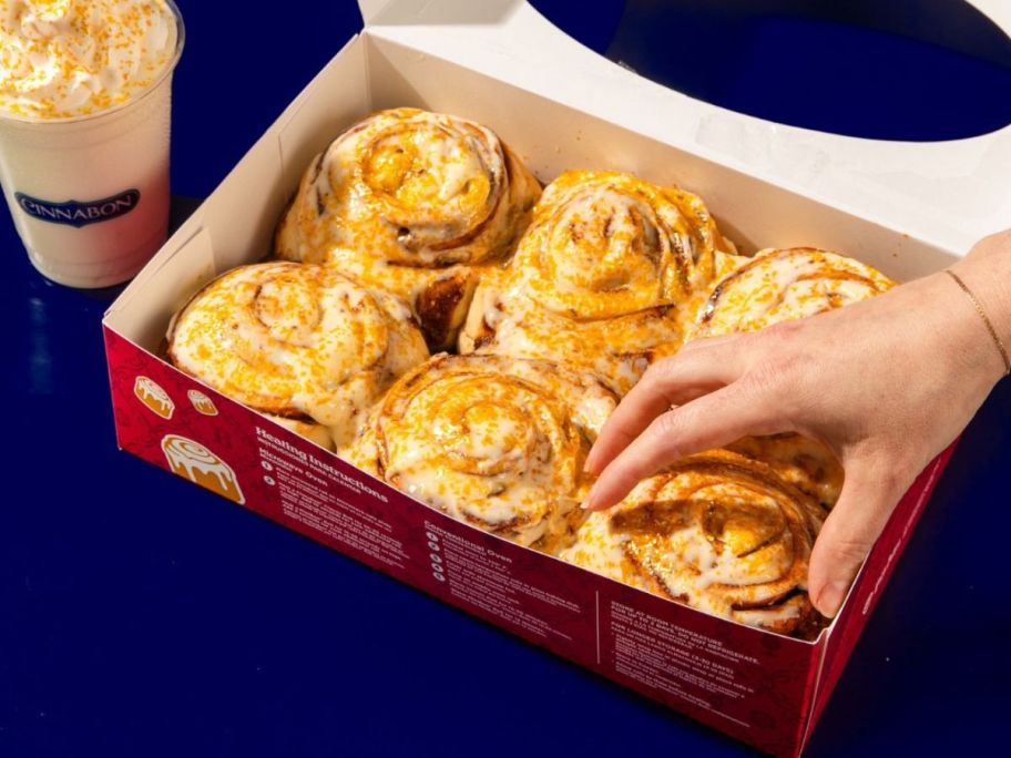 hand grabbing cinnabon butterbeer flavored roll from box