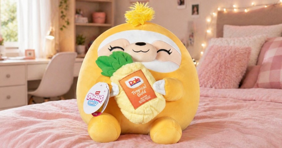 a Dole Pineapple plush stuffed toy on a pink bed