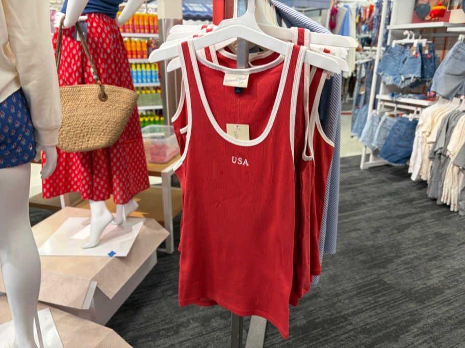 Red tank tops with "USA" text hang on a rack in a clothing store.