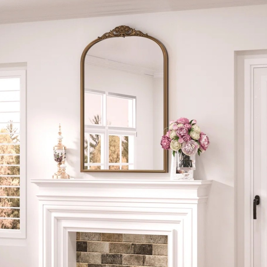 a gold framed arched mirro above a fire place
