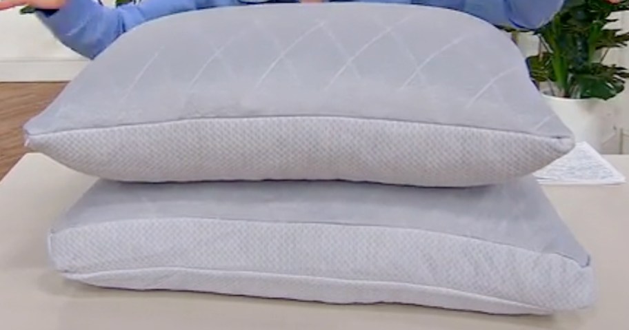 Two light gray pillows stacked on a table, featuring a quilted pattern on top and smooth edges.