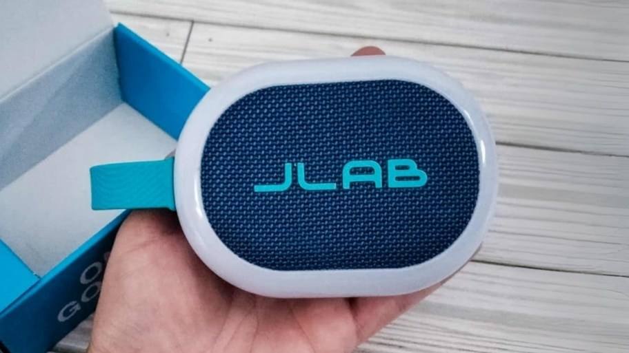 a mans hand holding a small bluetooth speaker