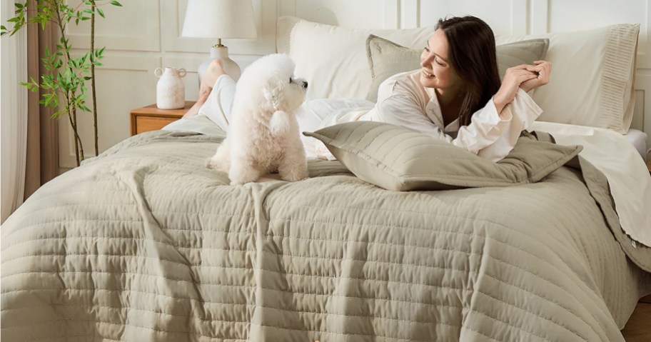 woman and dog laying on tan quilted blanket