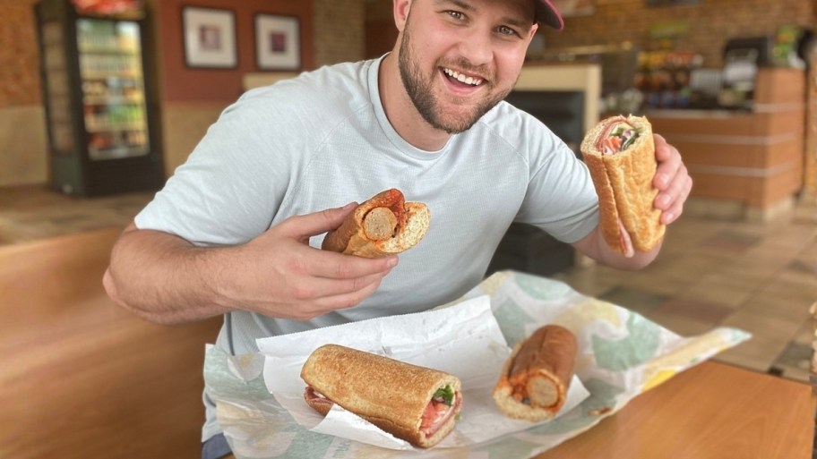 a man holding two subway sandwiches