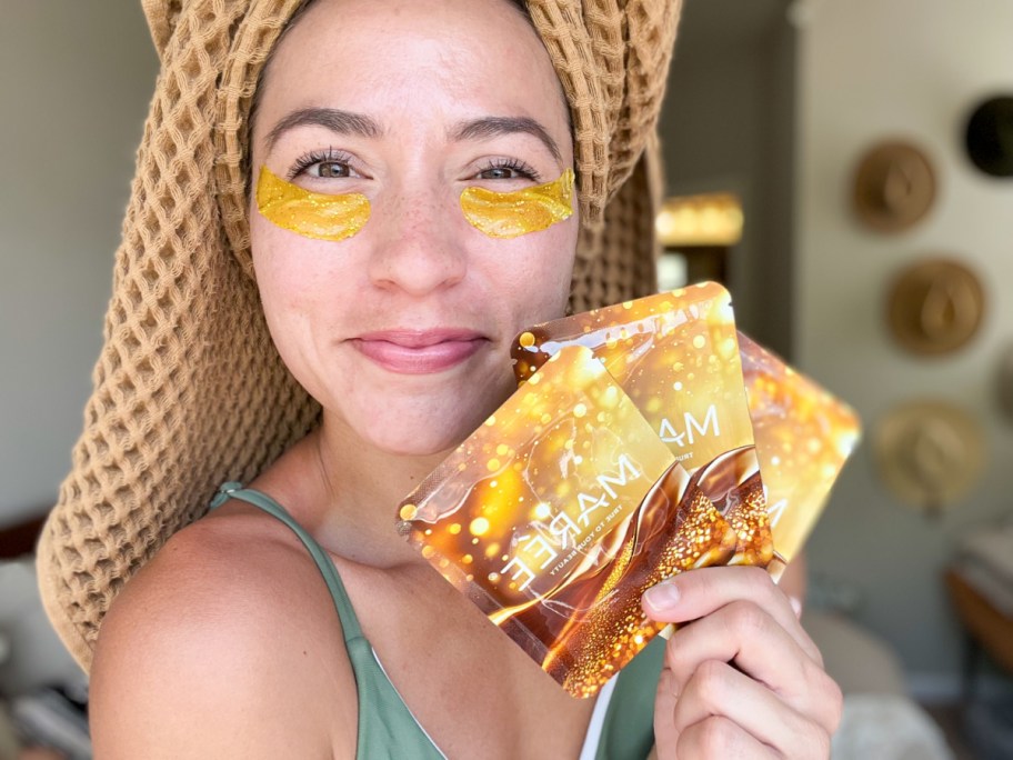 woman wearing gold under eye gels and holding gold packages of under eye gels