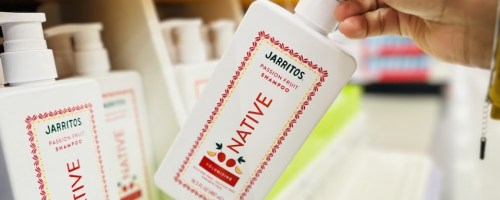 woamns hand holding a bottle of native shampoo