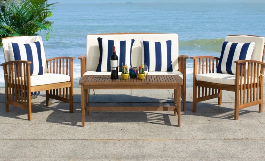 acia wood patio set with white and blue pillows next to beach