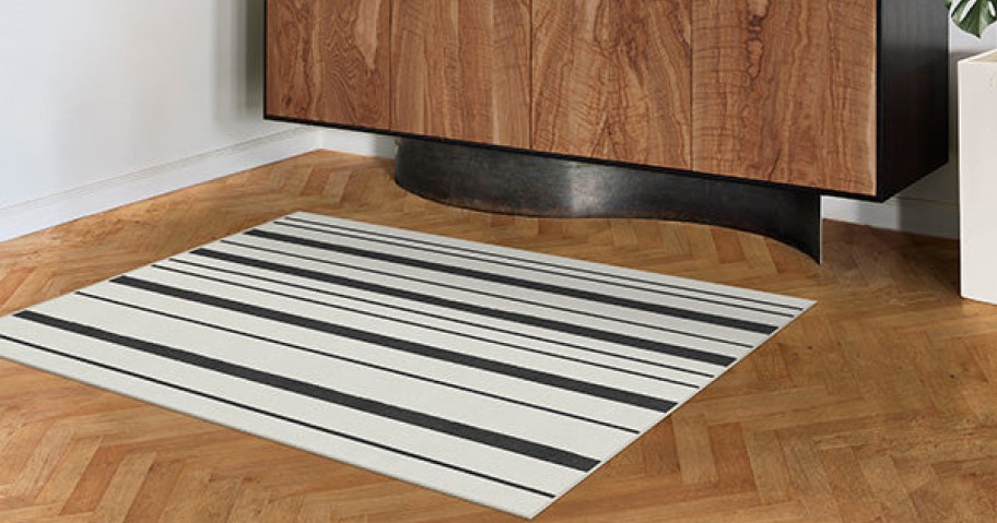 A striped rug on a wooden floor, with a piece of furniture in the background.