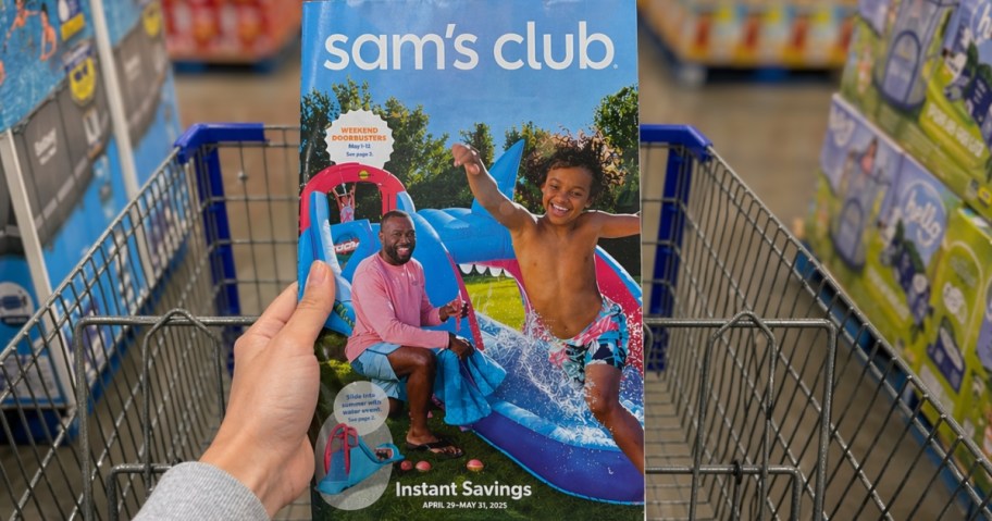 hand holding a Sam's Club Instant Savings brochure with a Sam's Cart behind it
