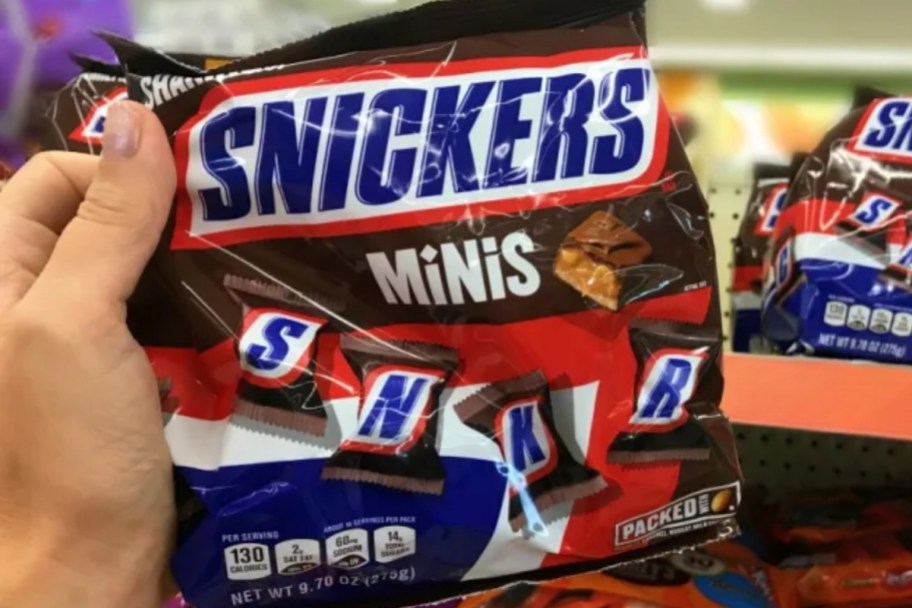 mans hand holding a bag of snickers mini candy bars