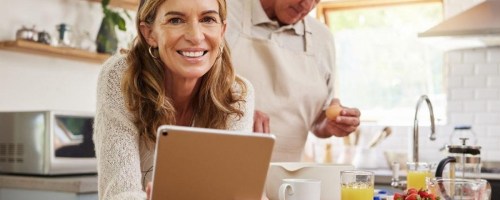 woman holding an iPad next to a man making food in a kitchen