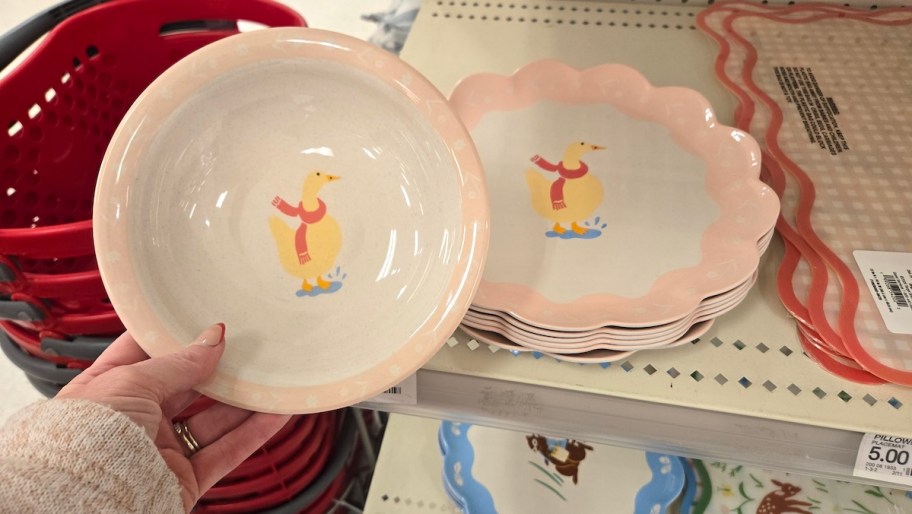 hand holding goose pink bowl in front of stack of goose plates on shelf