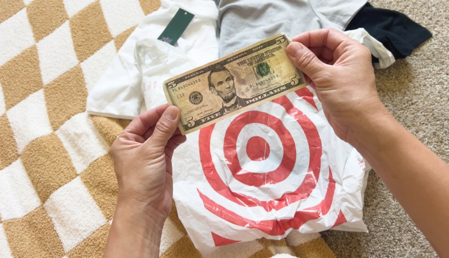 person holding a five dollar bill over a target shopping bag