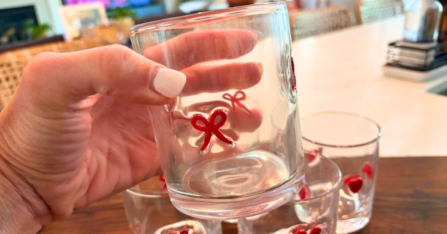 hand holding a glass tumbler with bow icons on it