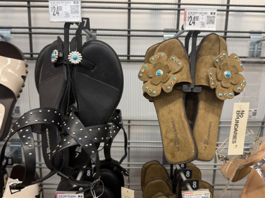 Two pairs of women's sandals are displayed on a rack. The black pair has studded straps and turquoise flower accents, while the brown pair features flower embellishments with turquoise centers.