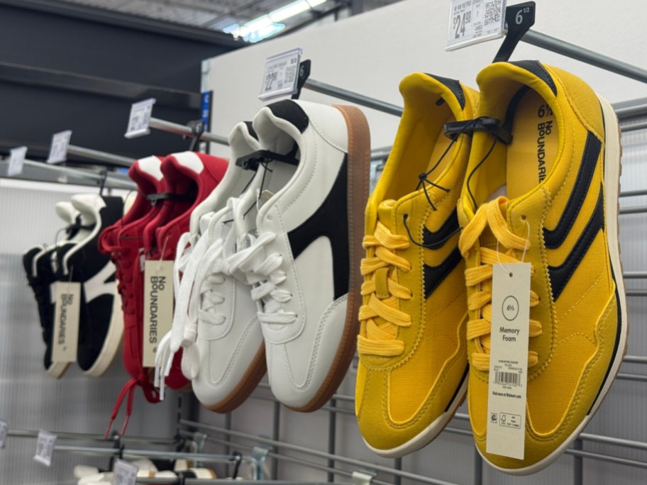 A row of colorful sneakers hangs on a rack in a store. Yellow, white, and red shoes.