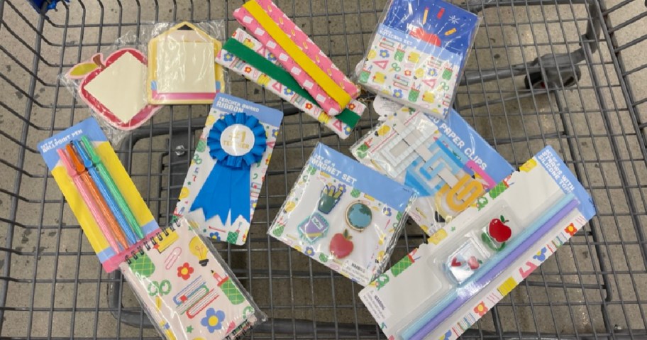 A shopping cart filled with colorful school supplies, including notebooks, pens, rulers, and stickers with playful designs.
