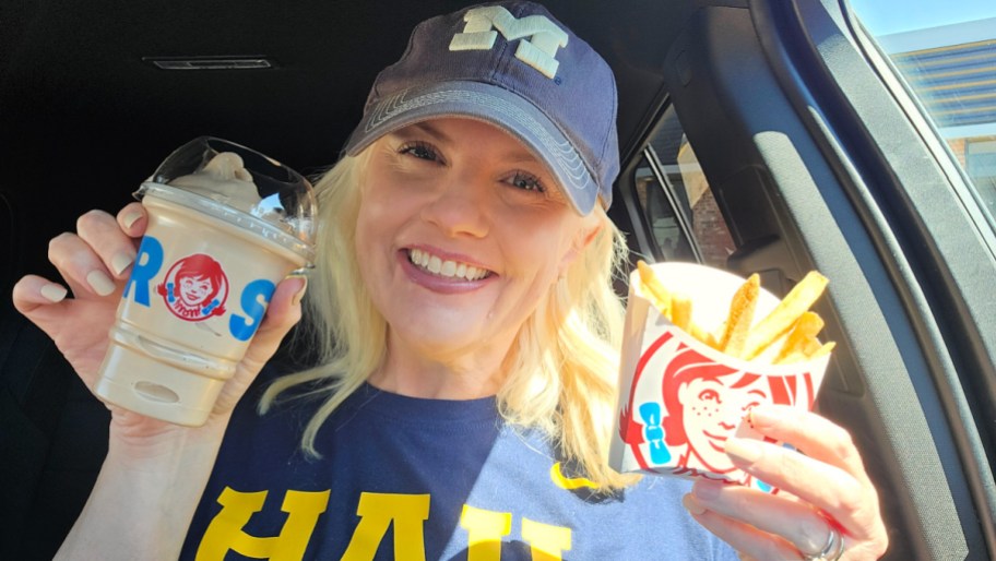 smiling woman sitting in a car and holding a wendy's frosty and fries