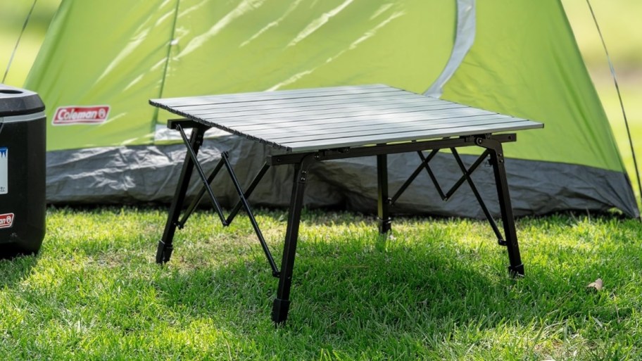 a gray camping table set up in front of a tent at a camp site