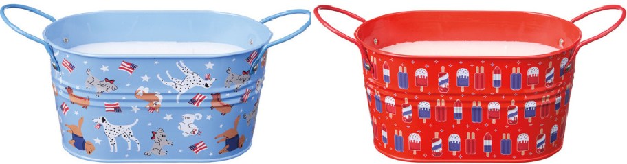 Two metal citronella candles: one blue with playful dogs, stars, and American flags; the other red with red, white, and blue popsicles. Both have handles.