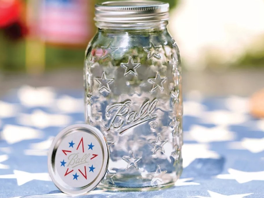ball mason jar with stars on jar and lid sitting on star tablecloth outside