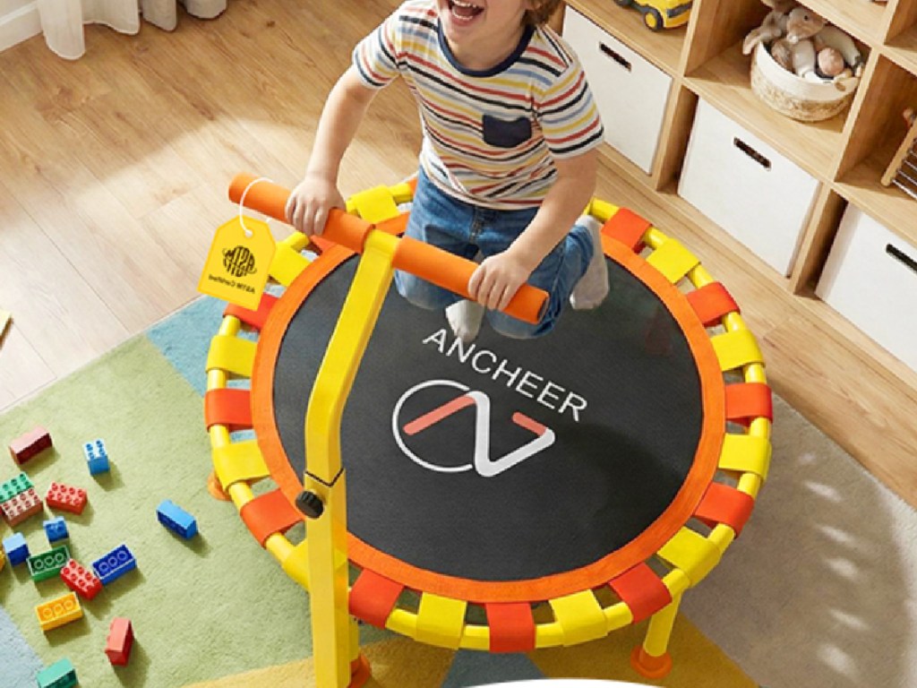 Little boy holding handle while jumping on mini trampoline