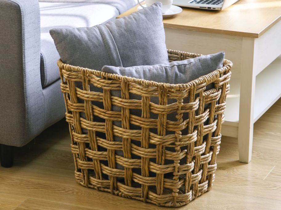 A large better homes and gardens storage basket with throw pillows in it